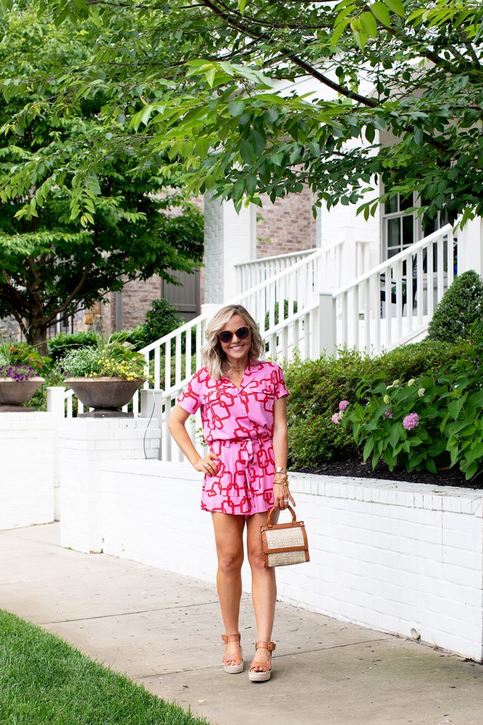 Gibson x Hi Sugarplum Summer of Color Collection by top us fashion blog, Hello Happiness: image of a smiling woman standing outside and wearing the Cavallo Notch Collar Button Down in Pink Chain, geometric cuff bracelets, Menorca Paper Bag Short in Pink Chain, Audrina sandals, Cosmo sunglasses, and holding a Deona crossbody bag. 