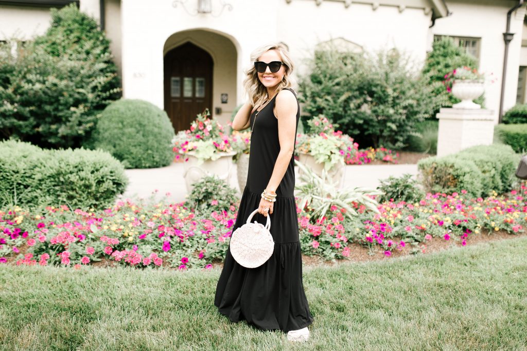 Walmart July Fashion... The Best Black Maxi Dress for Under $50, by popular Nashville fashion blog, Hello Happiness: image of a woman standing outside in front of a white stucco house with pink flower garden beds.  Woman is wearing a black Walmart Women's Hazel Maxi Dress, Women's Circus by Sam Edelman Nicola Bow Slide Sandals, Le Specs sunglasses, and holding a Eliza May Rose Compass Bag.    