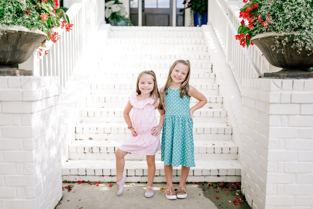 Trend Setting Back-to-School Outfits from Walmart by popular Nashville fashion blog, Hello Happiness: image of two girls standing outside their house wearing a Walmart Dex Girl's Printed A-Line Dress, Wonder Nation Casual Ruffle Chambray Dress, Wonder Nation Girls' Casual Ruffle Slip On Sneaker, and Wonder Nation Children's Casual Jelly Shoe. 