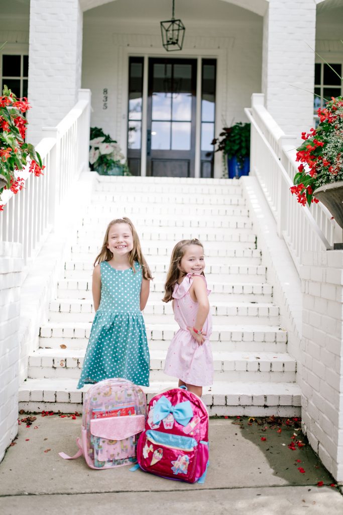 Trend Setting Back-to-School Outfits from Walmart by popular Nashville fashion blog, Hello Happiness: image of two girls standing outside their house wearing a Walmart Dex Girl's Printed A-Line Dress, Wonder Nation Casual Ruffle Chambray Dress, Wonder Nation Girls' Casual Ruffle Slip On Sneaker, and Wonder Nation Children's Casual Jelly Shoe.
