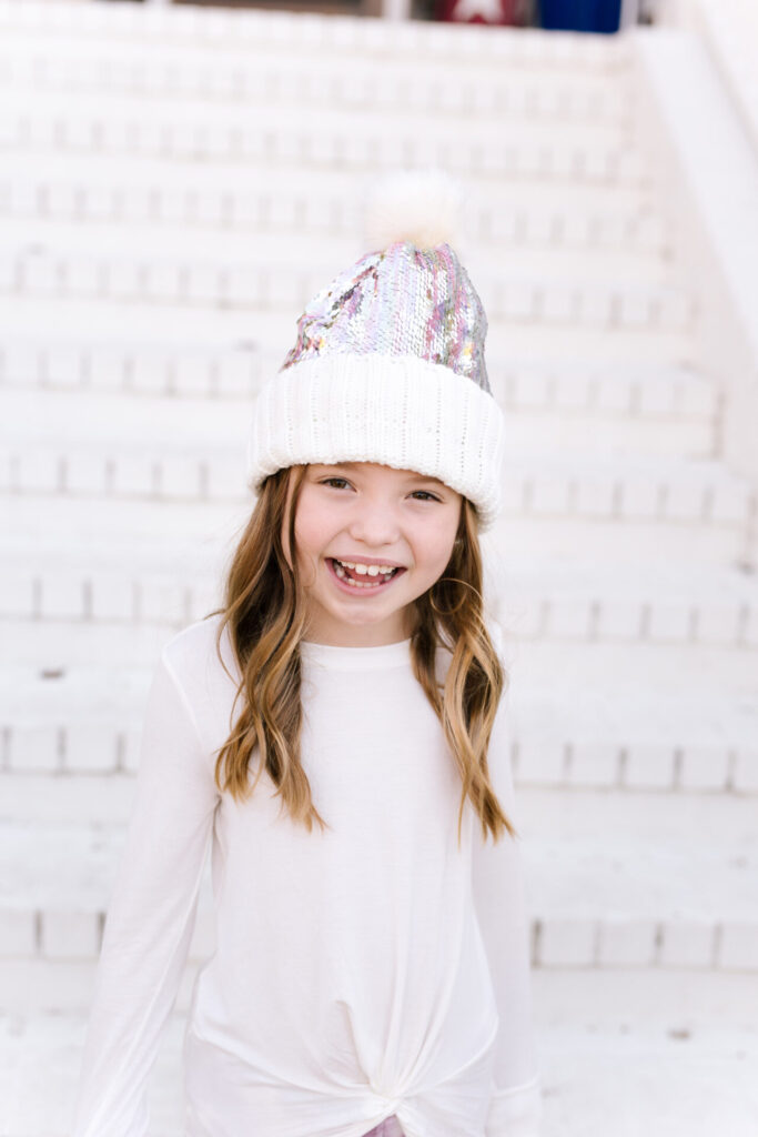 Nordstrom Fashion by popular Nashville fashion blog, Hello Happiness: image of a girl sitting on a white brick wall and wearing a Tucker and Tate sequin pom beanie, Nordstrom Zella Kids' Tie Dye Joggers, and Zella Kids' Peaceful Twist Front T-Shirt.