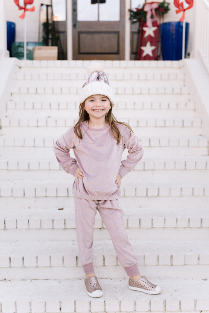 Nordstrom Fashion by popular Nashville fashion blog, Hello Happiness: image of a girl sitting on a white brick wall and wearing a Tucker and Tate sequin pom beanie, Nordstrom Zella Girl Kids' Cozy Active Pullover, and Nordstrom Zella Girl Kids' Velour Cozy Active Joggers.