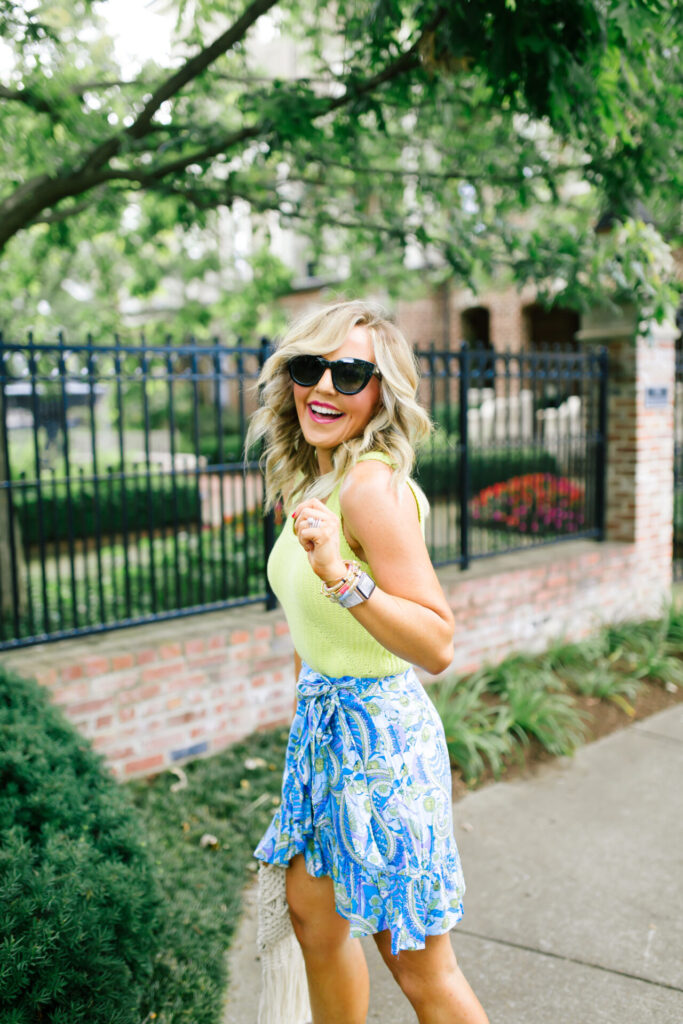 Walmart Scoop by popular Nashville fashion blog, Hello Happiness: image of a woman standing outside and wearing a Walmart Scoop Women’s Sweater Tank Top, Walmart Scoop Women's Short Wrap Skirt with Ruffle Hem, Walmart Scoop Macrame Wooden Handle Tote Bag, Walmart SODA Issue-s Casual Espadrilles Jute with Woods Open Toe Buckle Ankle Strap Wedge Sandal Shoes, and Walmart SA106 Thick Plastic Frame Round Horned Sunglasses for Women - Black.