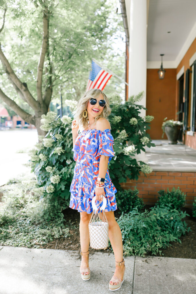 Buddy Love by popular Nashville fashion blog, Hello Happiness: image of a woman standing outside and wearing a BUDDYLOVE KIERA RUFFLED OFF THE SHOULDER MINI DRESS - FIREWORKS, Miuco Women Nets Bucket Handbags Straw Tote Bag Purses, See by Chloe Glyn Wedge Espadrilles, BIG LOVE sunglasses, and Lisi Lerch MARY - GOLD earrings. 
