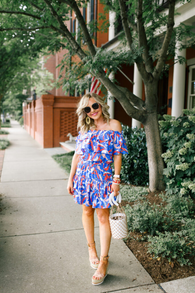 Buddy Love by popular Nashville fashion blog, Hello Happiness: image of a woman standing outside and wearing a BUDDYLOVE KIERA RUFFLED OFF THE SHOULDER MINI DRESS - FIREWORKS, Miuco Women Nets Bucket Handbags Straw Tote Bag Purses, See by Chloe Glyn Wedge Espadrilles, BIG LOVE sunglasses, and Lisi Lerch MARY - GOLD earrings. 