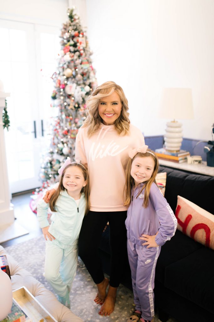 Everything Holiday with Academy Sports + Outdoors Gifts by popular life and style blog, Hello Happiness: image of a mom standing with her two daughters ad wearing Academy Sports + Outdoors Nike Girls' Logo Taping Track Suit Set, Nike Women's One Tights, and Nike Women's Therma Swoosh Training Hoodie.