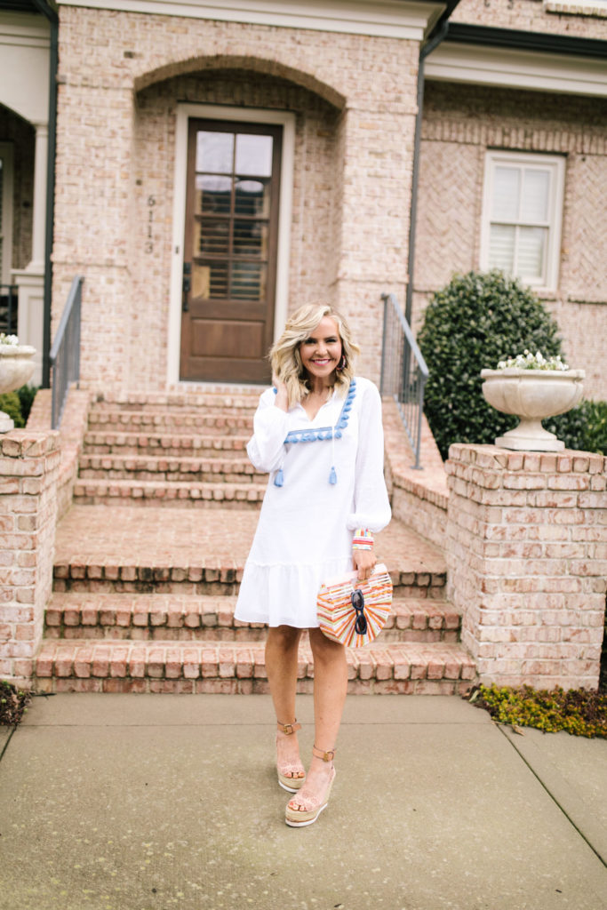 Sail to Sable by popular Nashville fashion blog, Hello Happiness: image of a woman wearing a Sail to Sable TASSEL FRONT FLOUNCE DRESS, See by Chloe Glyn Wedge Espadrilles, Candy Baublez custom stacks, Amazon Beauty YaYa Womens Bamboo/Acrylic Clutch Handbag Wooden Purse, Etsy Kristin Fast Limited Hoop Earrings, and Amazon zeroUV - Retro Oversized Square Sunglasses.