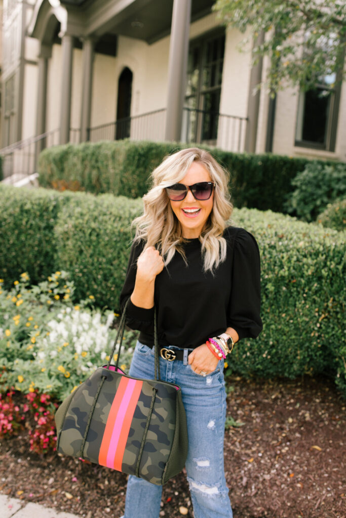 Social Threads by popular Nashville fashion blog, Hello Happiness: image of Natasha Stoneking standing outside and wearing a Amazon The Drop Women's Leona Short Puff Sleeve Crew Neck French Terry Sweatshirt, Social Threads Just Black Distressed Crop Kick Flare, Dillard's GB Here-4It Cheetah Print Haircalf Sneakers, and holding a Social Threads Hello Happiness Camo Striped Neoprene Tote.