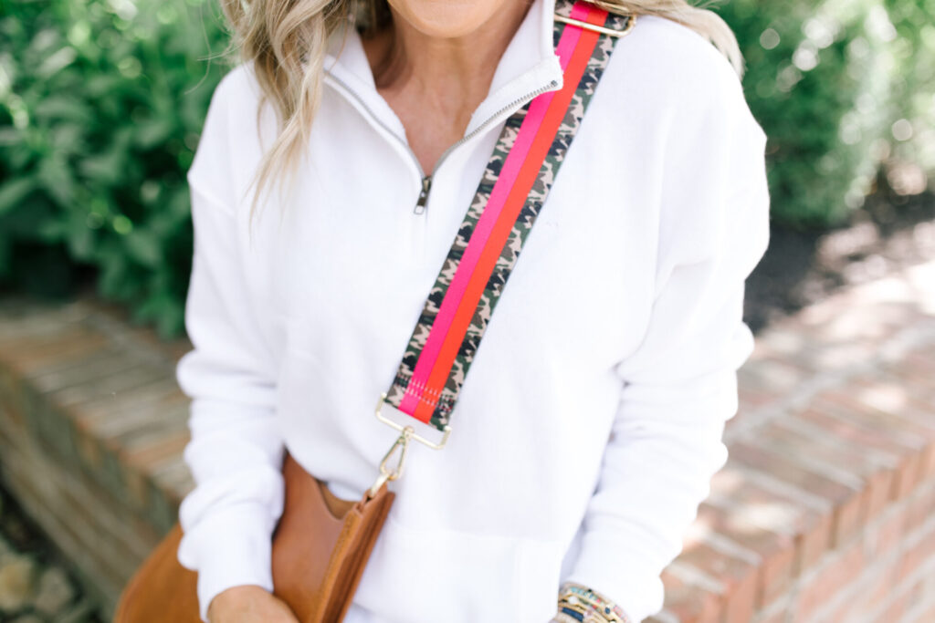 Social Threads by popular Nashville fashion blog, Hello Happiness: image of Natasha Stoneking wearing a Social Threads Ocean Drive Half Zip Sweatshirt, Social Threads Free People CRVY High Rise Cut Offs, Steve Madden TORIN WHITE WITH STUDS sneakers, and carrying a Social Threads Vegan Messenger Bag with a Social Threads Hello Happiness Blogger Collaboration Bag Strap.