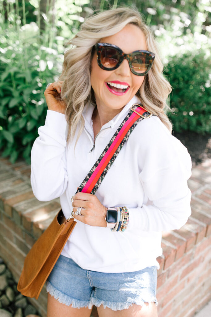 Social Threads by popular Nashville fashion blog, Hello Happiness: image of Natasha Stoneking wearing a Social Threads Ocean Drive Half Zip Sweatshirt, Social Threads Free People CRVY High Rise Cut Offs, Steve Madden TORIN WHITE WITH STUDS sneakers, and carrying a Social Threads Vegan Messenger Bag with a Social Threads Hello Happiness Blogger Collaboration Bag Strap.