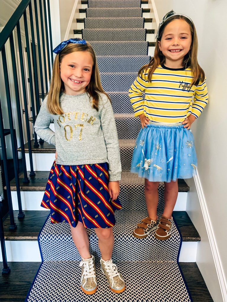 The Magical World of the Mini Boden Harry Potter Collection by popular Nashville fashion blog, Hello Happiness: image of two girls standing on a staircase and wearing Mini Boden Sequin Seeker Dress, Mini Boden High Tops, Mini Boden House Breton - Gryffindor Red/Gold long sleeve shirt, Mini Boden Hippogriff Tulle Skirt, Mini Boden Hippogriff Bomber Jacket, and Fun Low Tops.