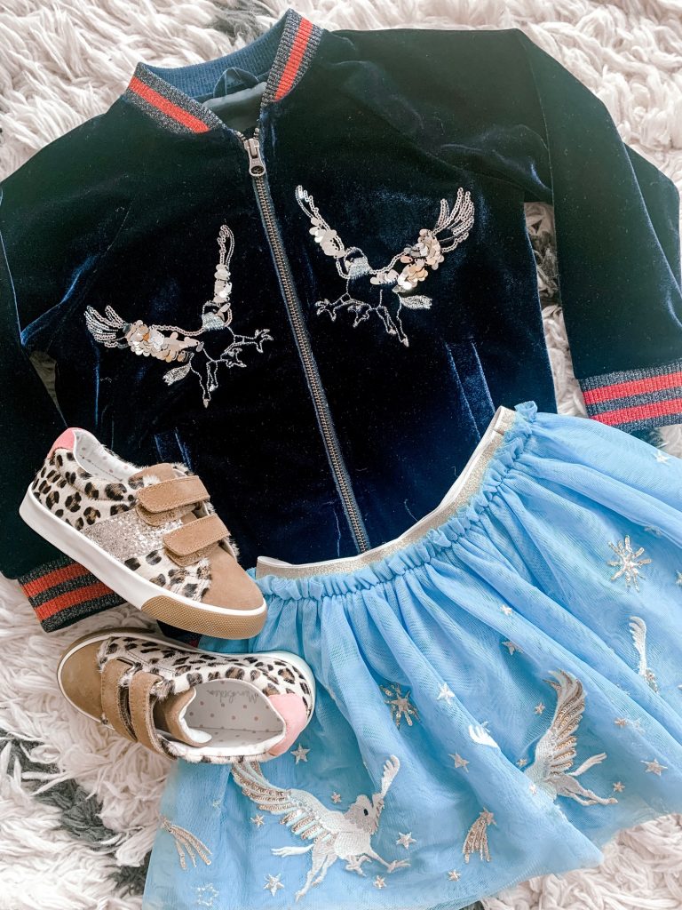 The Magical World of the Mini Boden Harry Potter Collection by popular Nashville fashion blog, Hello Happiness: image of a Mini Boden House Breton - Gryffindor Red/Gold long sleeve shirt, Mini Boden Hippogriff Tulle Skirt, Mini Boden Hippogriff Bomber Jacket, and Fun Low Tops.