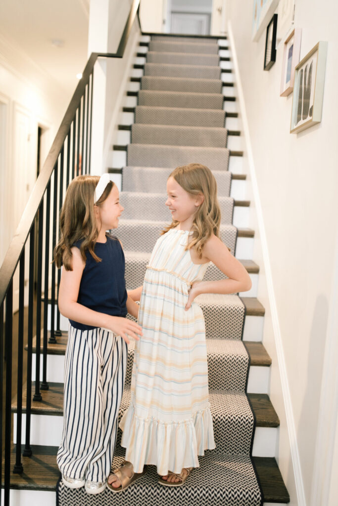 Walmart Back to School by popular Nashville life and style blog, Hello Happiness: image of two young girls standing on a stair case and wearing a Walmart Jessica Simpson Girls Sleeveless Twist Front Top and Paper Bag Pants, Walmart Wonder Nation Shining Star Low-Top Court Sneaker, Walmart Jessica Simpson Girls Halter Neck Striped Maxi Dress, and Walmart bebe Girls Big Kid Two Buckle Strap Cork Footbed Slide Sandals Rose Gold.