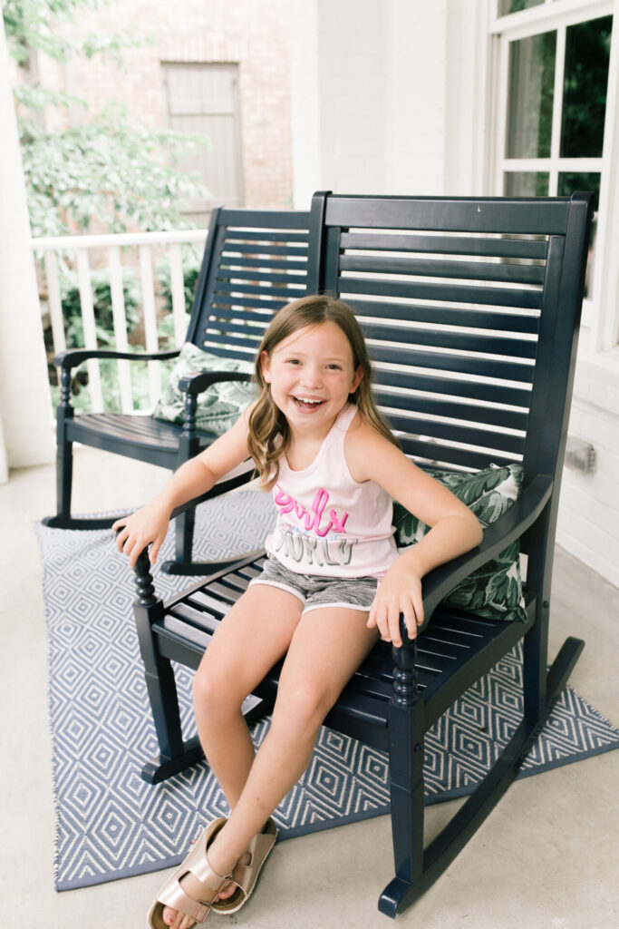 Walmart Back to School by popular Nashville life and style blog, Hello Happiness: image of a young girl sitting outside in a black rocking chair and wearing a Walmart Cheetah Girls Graphic Racerback Performance Tank Top and Running Shorts.