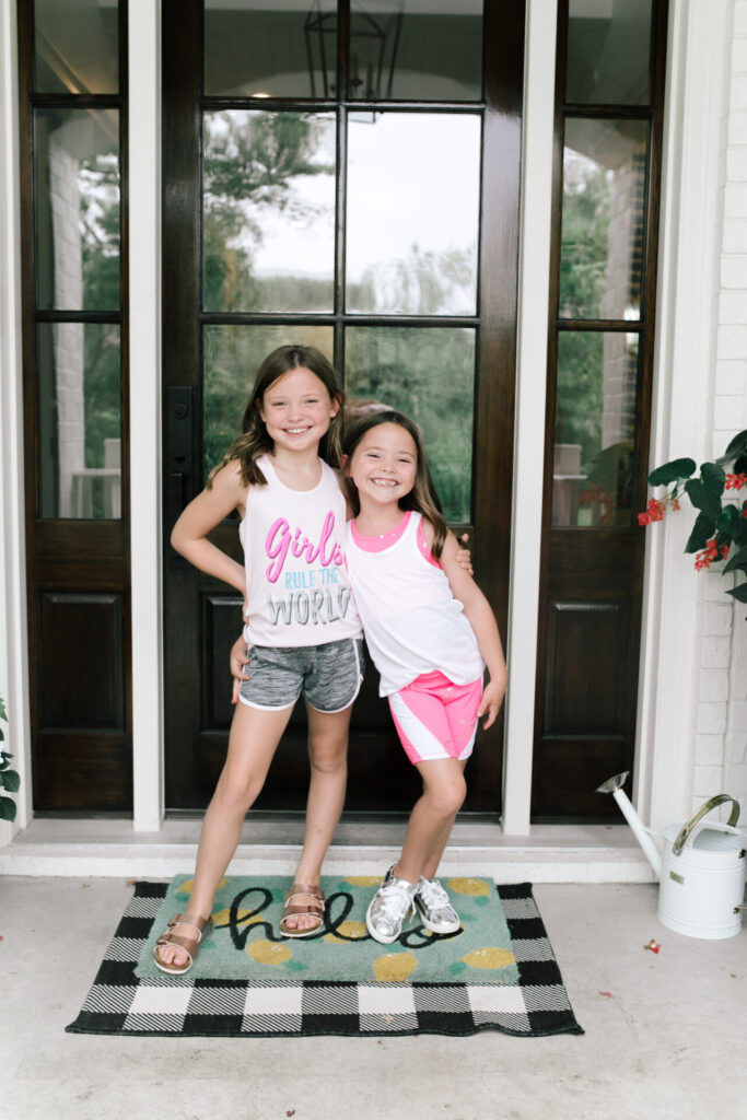 Walmart Back to School by popular Nashville life and style blog, Hello Happiness: image of two young girls standing outside and wearing a Walmart Cheetah Girls Graphic Racerback Performance Tank Top and Running Shorts and Walmart Athletic Works Girls Active 2-Fer Tank and Bike Printed Bike Shorts.