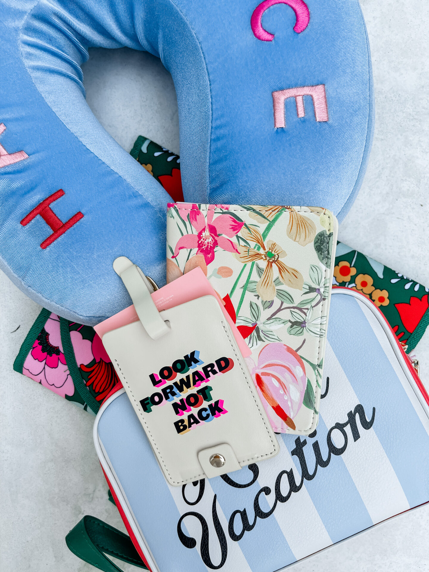 Traveling With Kids by popular Nashville travel blog, Hello Happiness: image of a neck pillow, floral print passport holder, and blue and white stripe bag. 