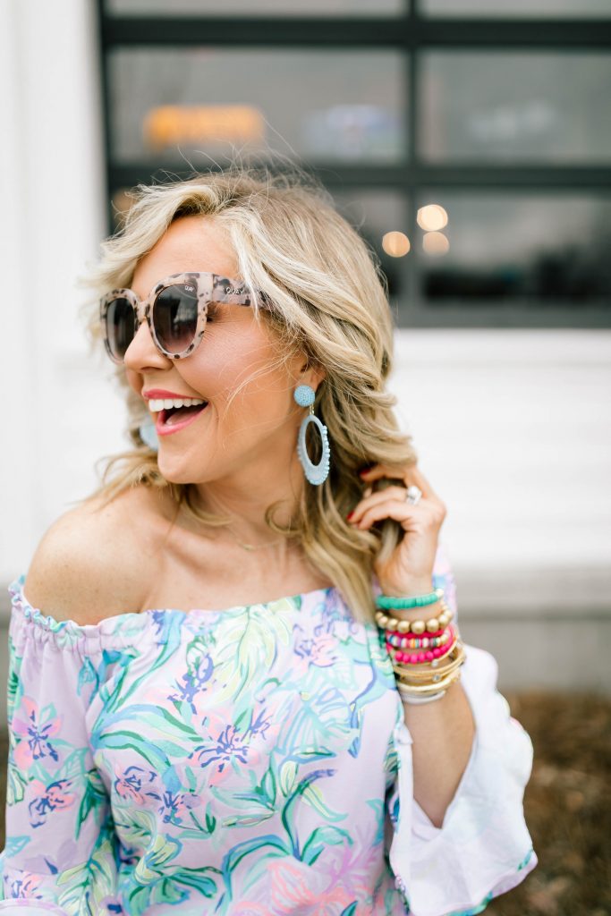 Hip Hip Hooray... The Lilly After Party Sale is Here! by popular Nashville fashion blog, Hello Happiness: image of a woman wearing a Lilly Pulitzer CALLA OFF-THE-SHOULDER ROMPER, STEVEN by Steve Madden Women's Sirena Espadrille Wedge Sandal, Amazon Straw Canteen Purse, Amazon I-BOSOM Colorful Boho Pom Pom Tassel Bag Charm Key Chain, and Nordstrom Quay Australiax JLO Limelight 54mm Oversize Sunglasses. 