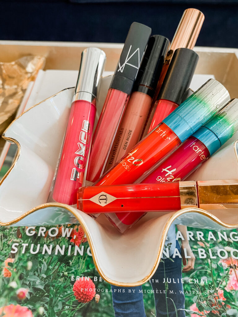 Spring Lip Glosses by popular Nashville beauty blog, Hello Happiness: image of a white ceramic trinket dish filled with various red and pink lip glosses.