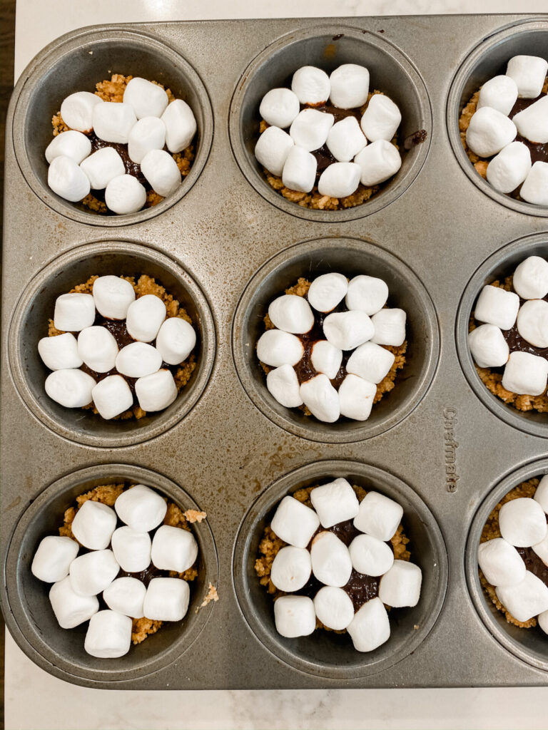 Frozen S'mores Cups by popular Nashville lifestyle blog, Hello Happiness: image of the graham cracker crusts topped with chocolate and mini marshmallows in muffin tins. 