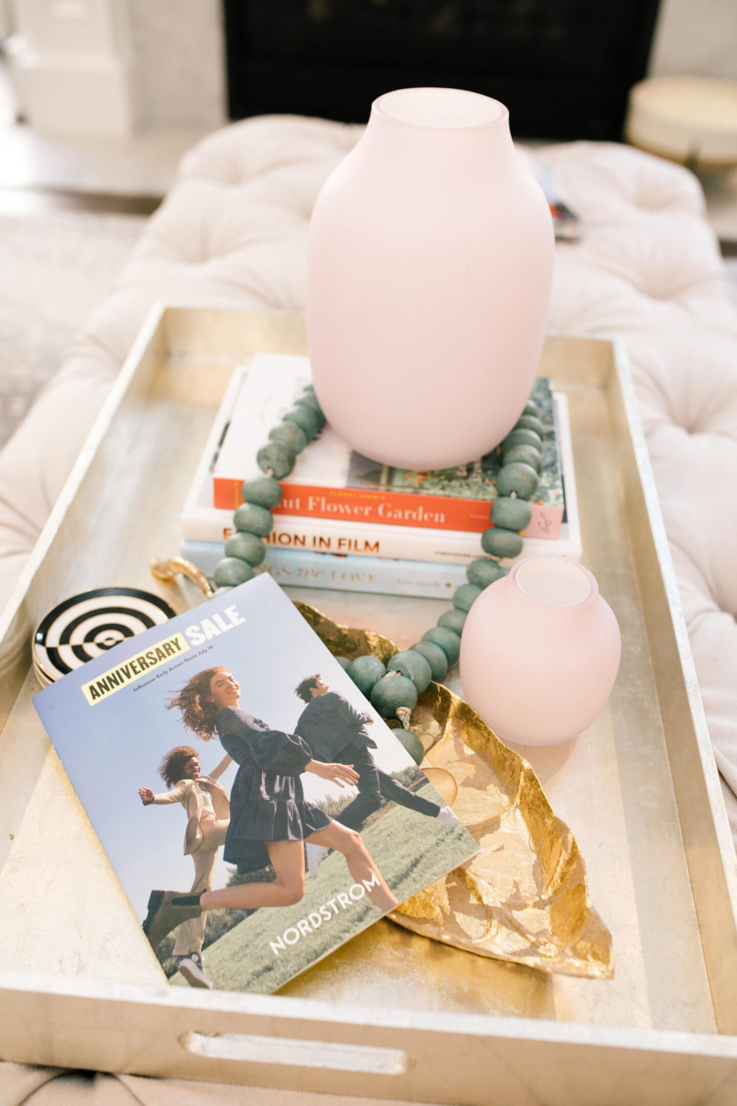 Nordstrom Anniversary Sale by popular Nashville fashion blog, Hello Happiness: image of a Nordstrom Anniversary Sale catalog on a wooden serving dray decorated with coffee table books, black and white coasters, gold leaf tray, green wooden bead garland, and pink vases. 