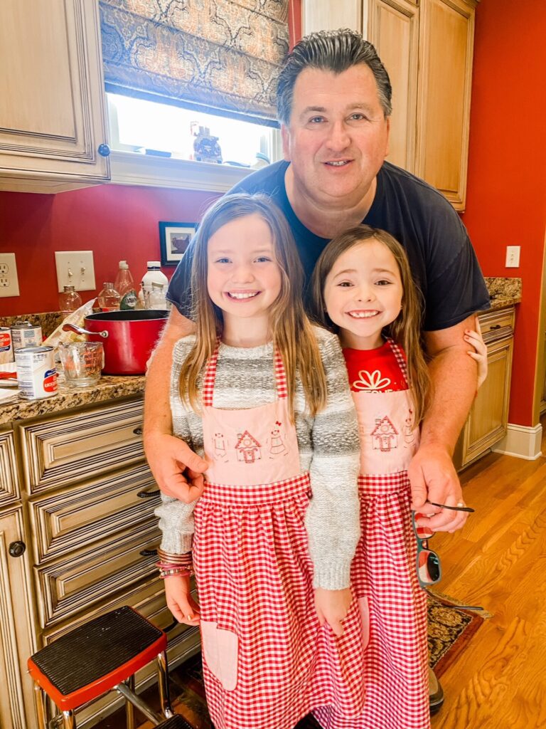 Year in Review by popular Nashville lifestyle blog, Hello Happiness: image of two young girls standing n the kitchen with their grandpa and wearing matching red aprons. 