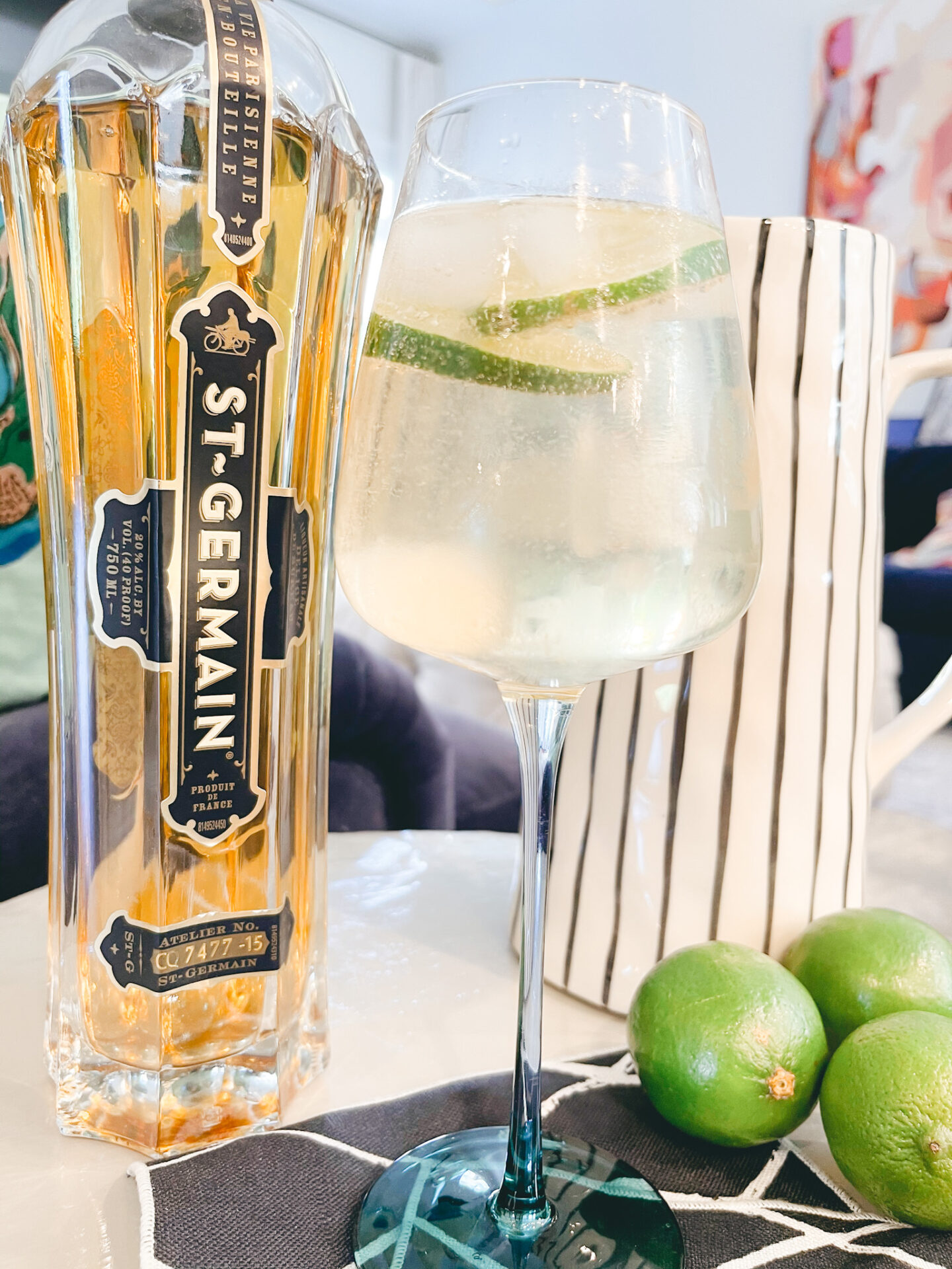 Hugo Cocktail by popular Nashville lifestyle blog, Hello Happiness: image of St. Germain, a wine glass limes, black and white stripe linen napkins, and a gold and white stripe pitchers. 