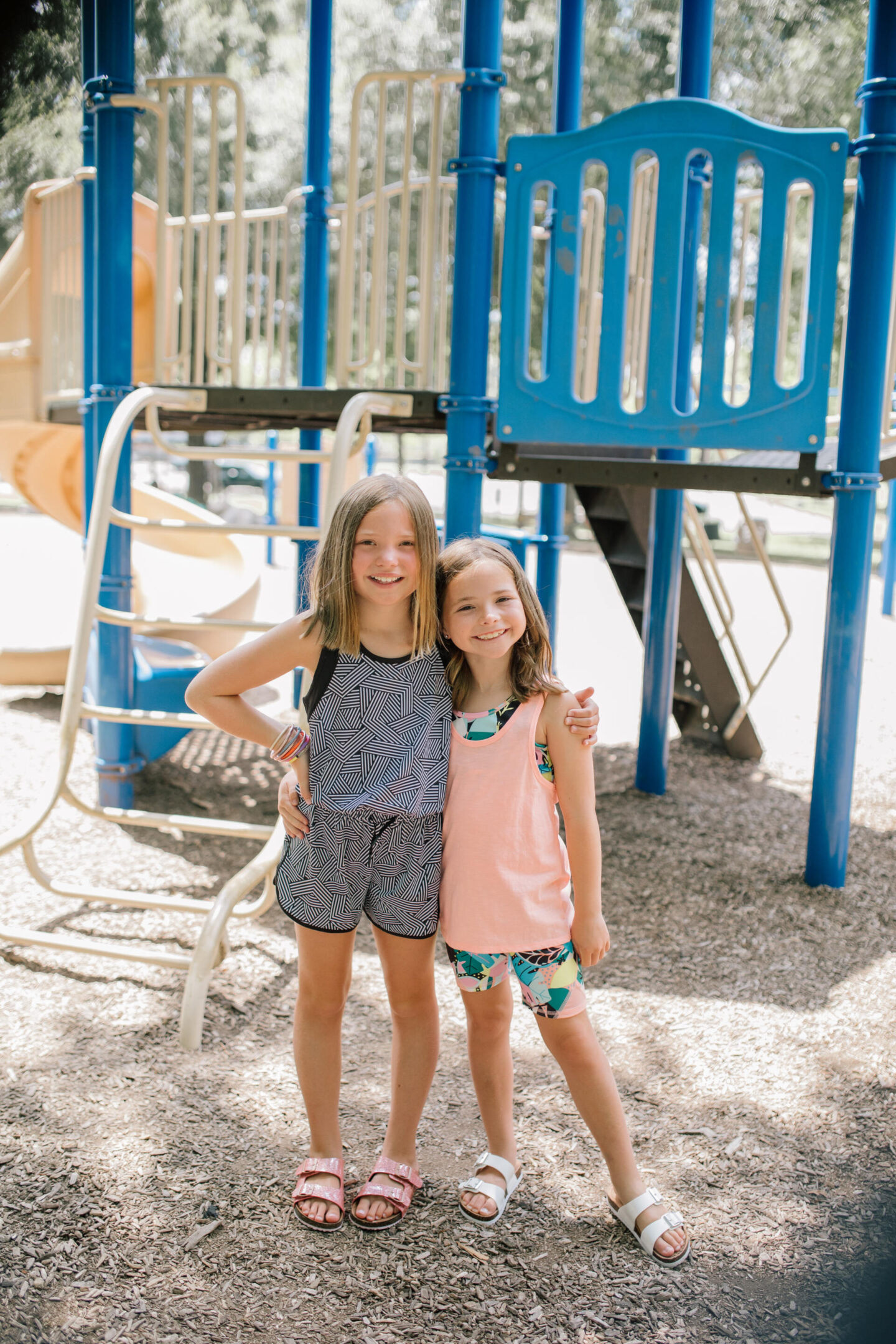 Back to School Essentials by popular Nashville lifestyle blog, Hello Happiness: image of two young girls standing together and wearing a black and white geometric tank top, black and white geometric print shorts, pink shimmer strap sandals, tropical print sports bra, peach tank top, tropical print shots and white strap sandals. 