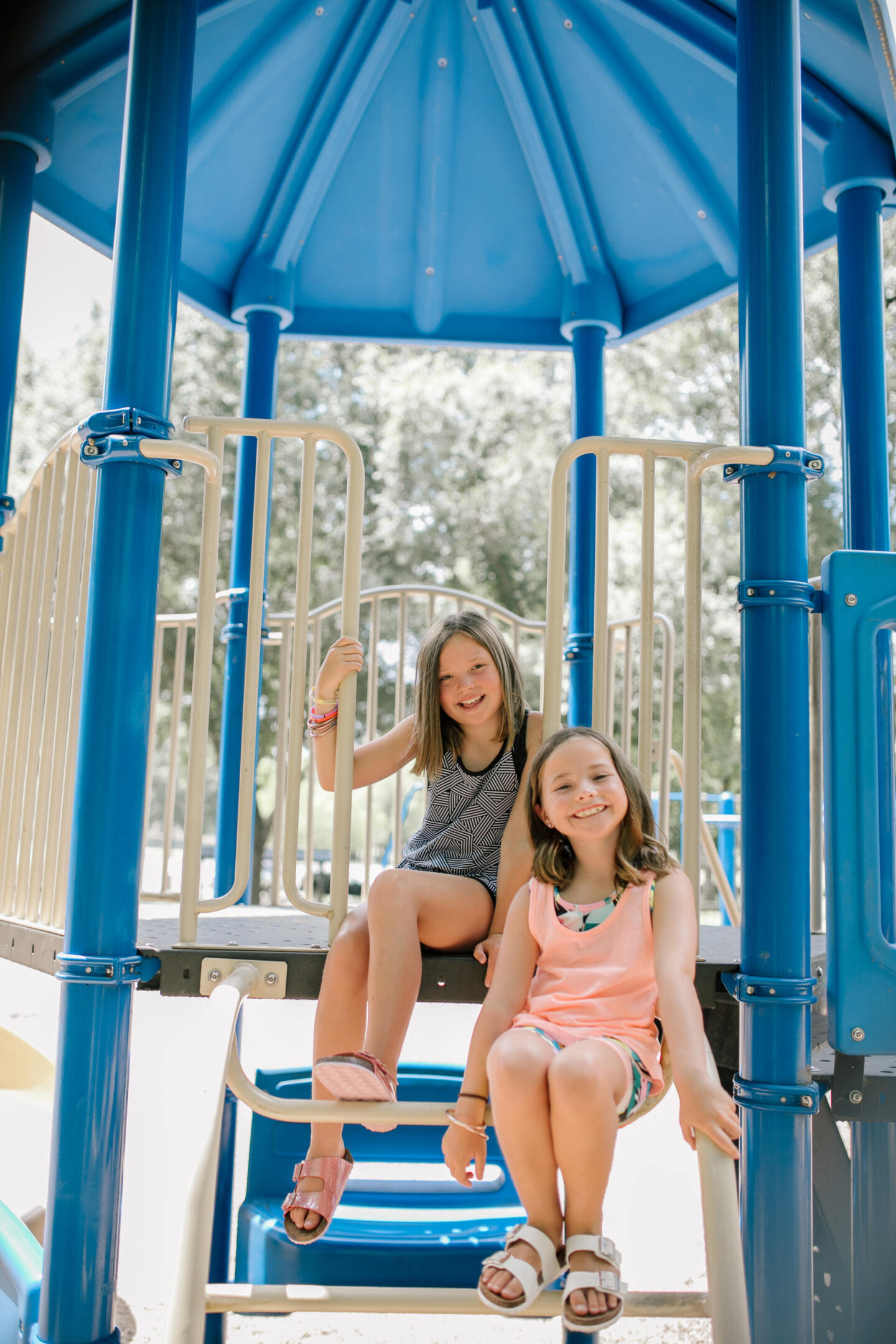 Back to School Essentials by popular Nashville lifestyle blog, Hello Happiness: image of two young girls standing together and wearing a black and white geometric tank top, black and white geometric print shorts, pink shimmer strap sandals, tropical print sports bra, peach tank top, tropical print shots and white strap sandals. 