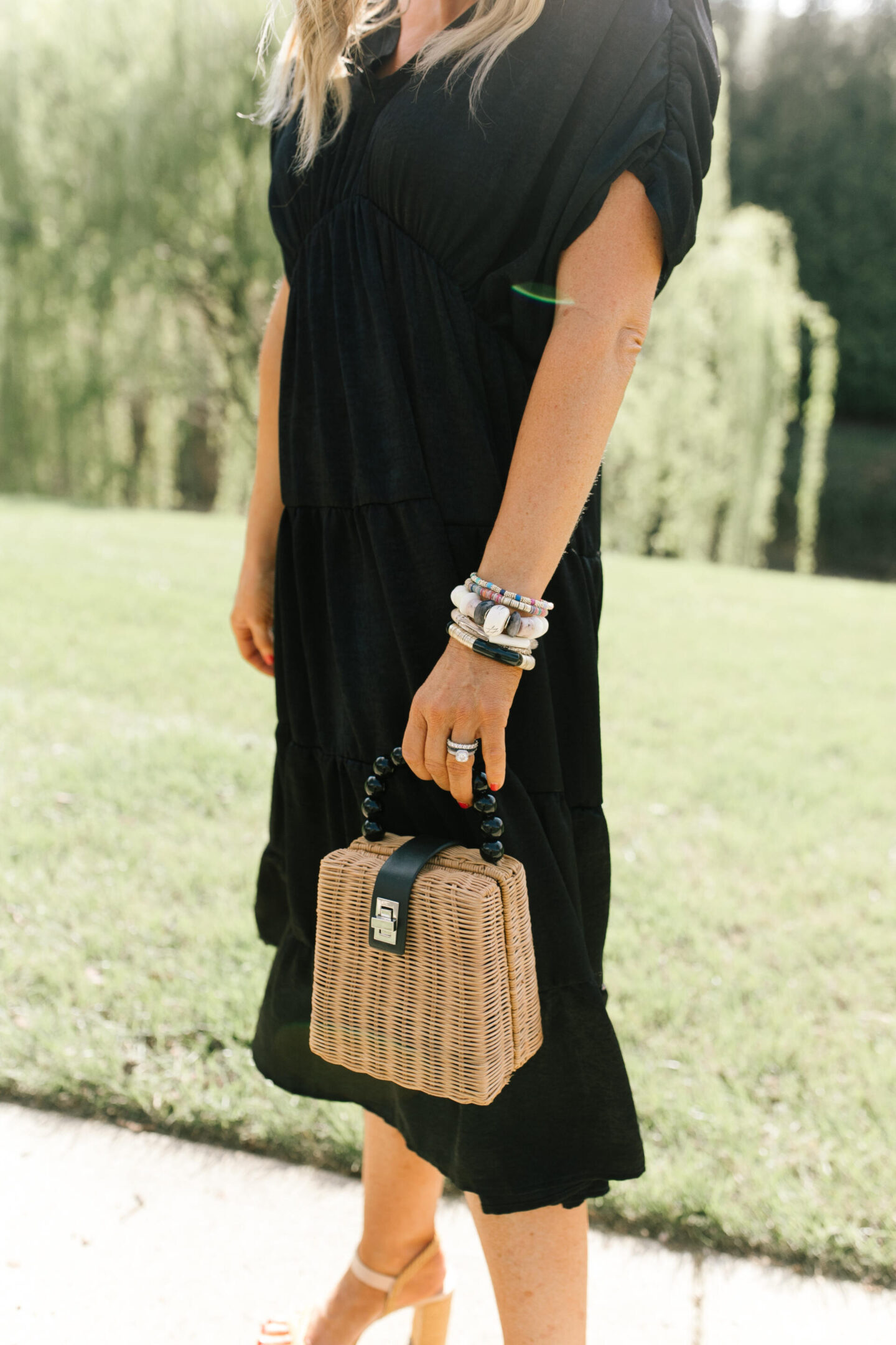 Summer Dresses by popular Nashville of Natasha Stoneking wearing a shirred tiered midi dress, after hours sunglasses, platform wedge sandals, and holding a woven bucket bag. 