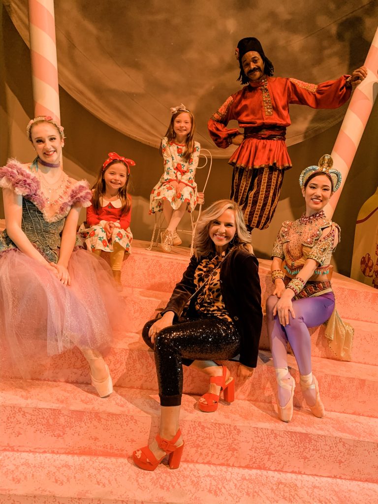 All Our Favorite Family Holiday Traditions by popular life and style blog, Hello Happiness: image of two girls and their mom sitting with ballet dancers and wearing Eleanor Rose Christmas Rose dresses. 