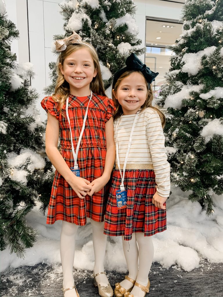 All Our Favorite Family Holiday Traditions by popular life and style blog, Hello Happiness: image of two girls at Santa's flight academy and wearing J. Crew Girls' smocked flutter-sleeve dress in red Stewart tartan, Amazon mini melissa Kids' Mini Ultragirl Special Ballet Flat, J. Crew Girls' velvet bow headband, and J. Crew Girls mixy dress in Stewart tartan.