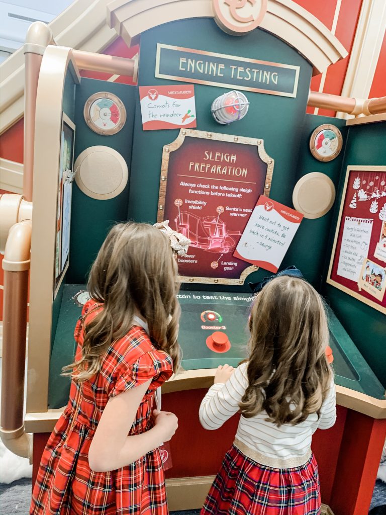 All Our Favorite Family Holiday Traditions by popular life and style blog, Hello Happiness: image of two girls at Santa's flight academy and wearing J. Crew Girls' smocked flutter-sleeve dress in red Stewart tartan, Amazon mini melissa Kids' Mini Ultragirl Special Ballet Flat, J. Crew Girls' velvet bow headband, and J. Crew Girls mixy dress in Stewart tartan.