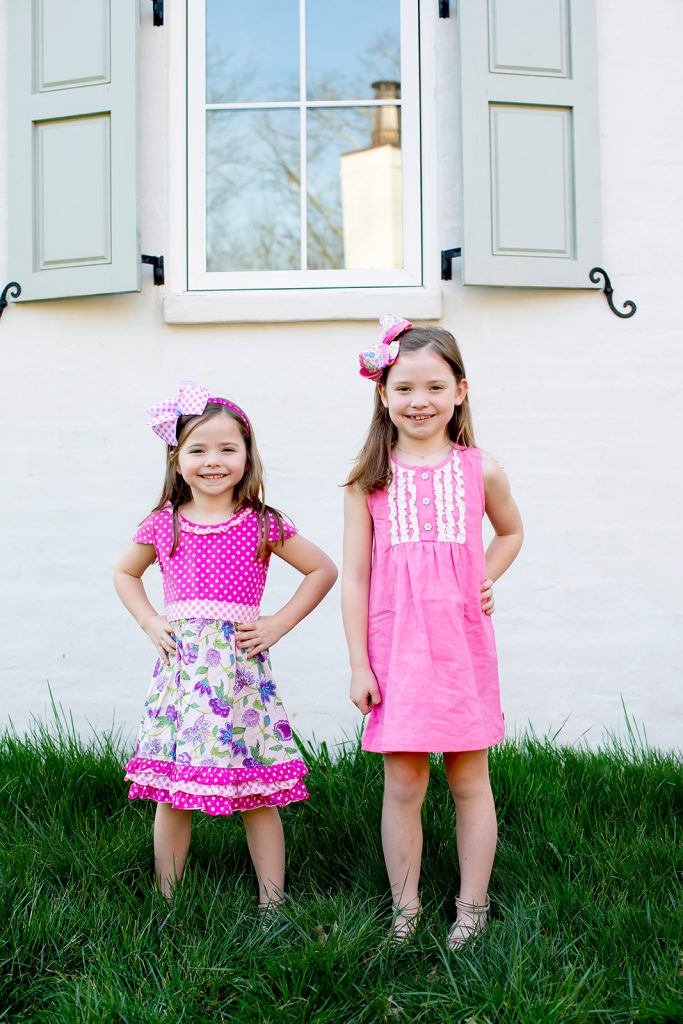 Ready, Set, SHOP! The Best in 4th of July Sales by popular Nashville fashion blog, Hello Happiness: image of two young girls standing outside in front of a white house with grey storm shutters wearing Matilda Jane Clothing Dazzling Dream Dress and Matilda Jane clothing Dot Dot Dot Dress.