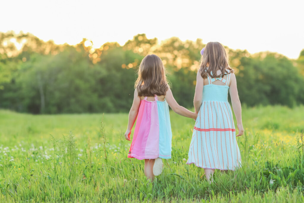 Summer Bucket List by popular Nashville lifestyle blog, Hello Happiness: image of two girls holding hands while walking in a grassy meadow and wearing Matilda Jane Clothing dresses. 